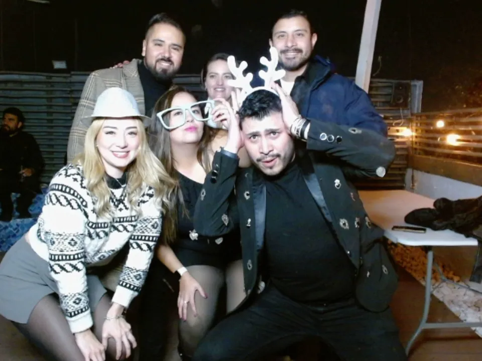 Invitados de una posada navideña sonriendo mientras esperan su impresión al momento en la cabina fotográfica Snap Memory.